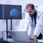 Doctor working on laptop with brain image in the background